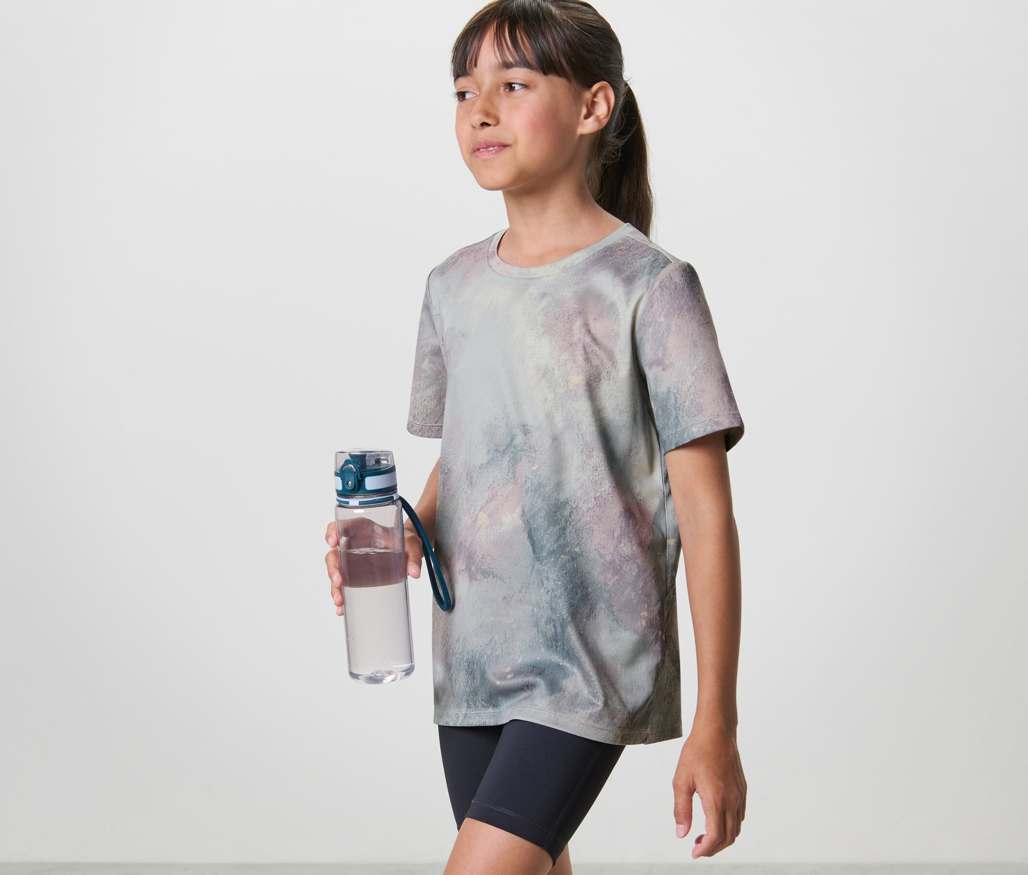 Une fille tient une gourde et porte un t-shirt de sport pour enfant (lot de 2).