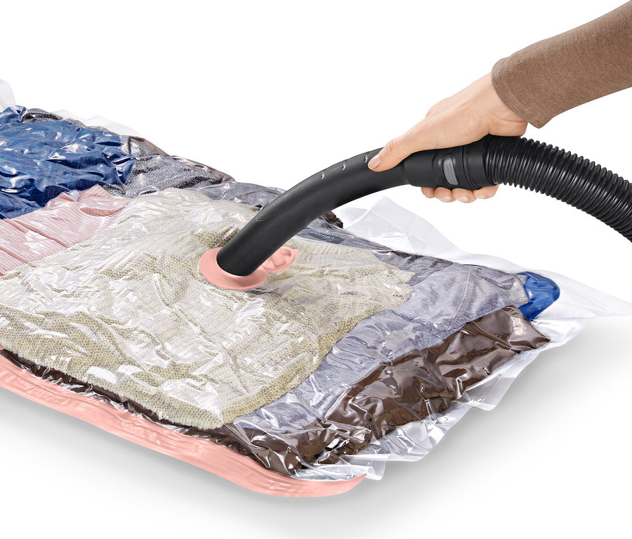 Une main utilise un tuyau d'aspirateur sur 2 sacs de rangement sous vide plats.