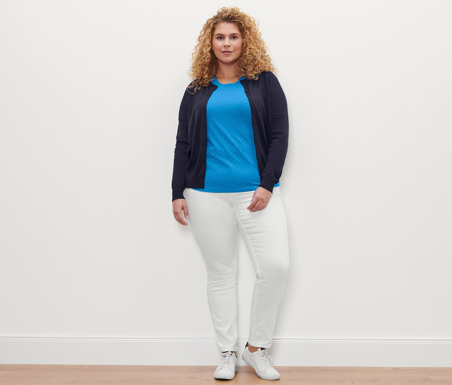 Une femme pose et porte un T-shirt à pois, un jean Colored Denim « Fit Emma » blanc crème et un cardigan en maille fine.