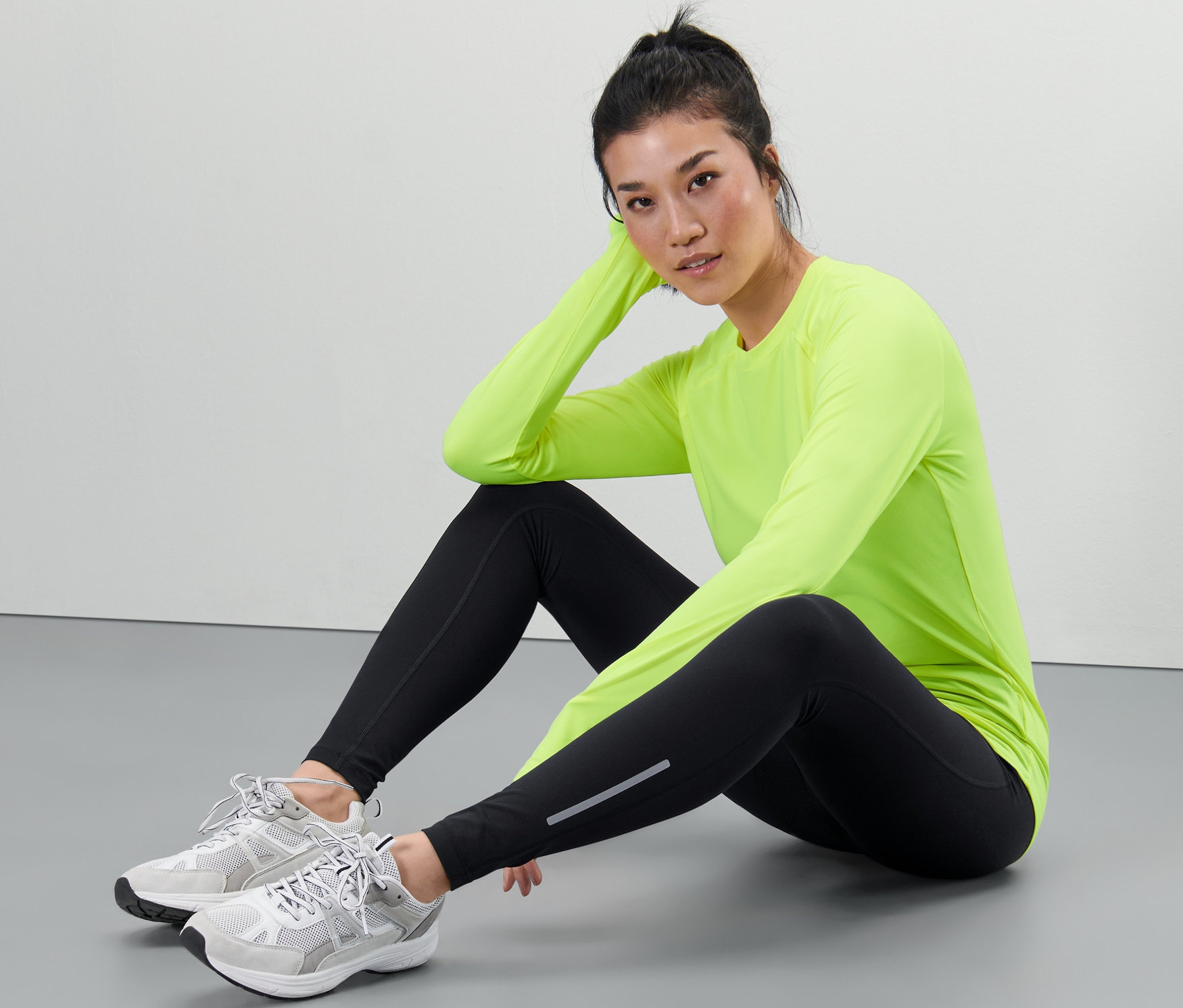 Femme assise par terre portant un legging de sport et un haut vert néon.