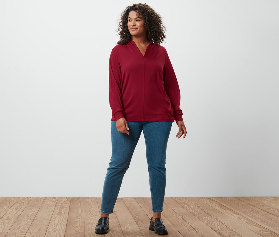 Une femme debout porte un t-shirt à manches longues avec encolure en V rouge bordeaux, un tregging « Fit Nelly » et des loafers en cuir.