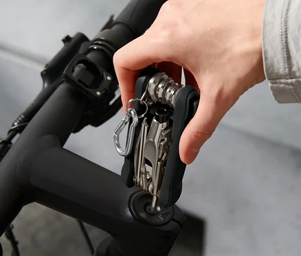 Une main tient un outil multifonctionnel pour vélo sur le guidon d'un vélo. Un casque est visible en arrière-plan.