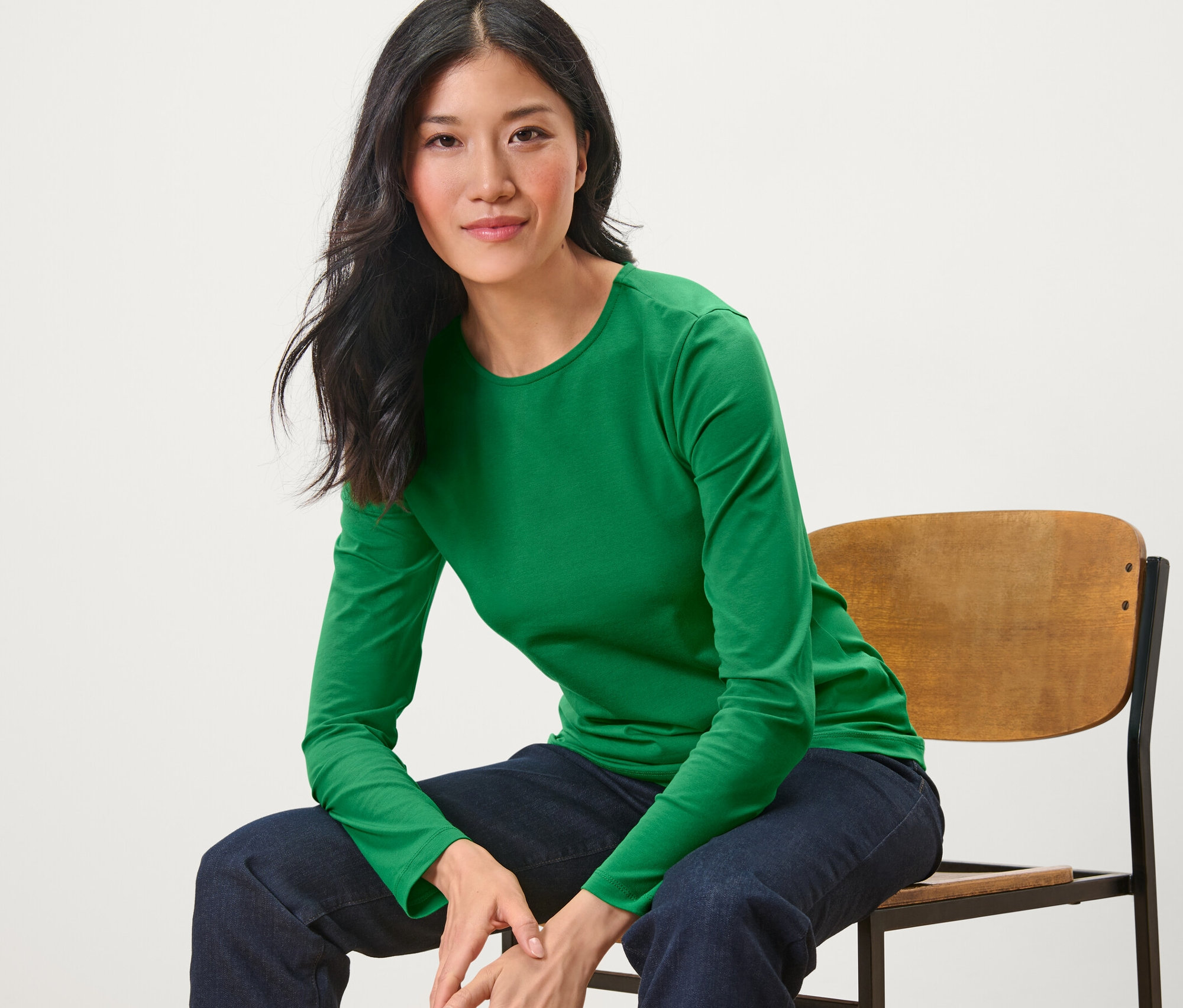 Une femme est assise sur une chaise et porte un haut manches longues vert.