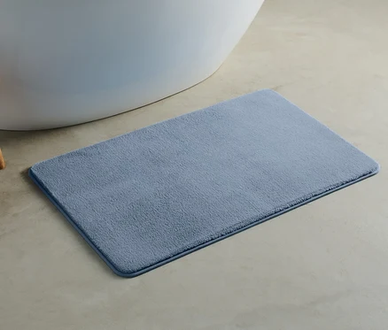 Un tapis de bain bleu d'environ 100 x 60 cm est posé sur le sol à côté d'une baignoire.