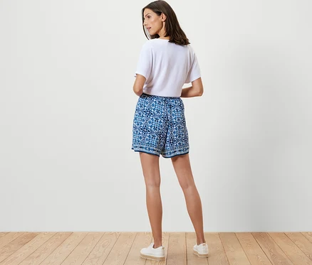 Une femme, vue de dos, porte un short tissé imprimé et un chemisier structuré blanc.