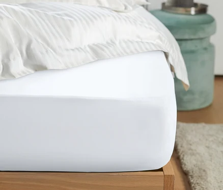 Gros plan d'un drap-housse en jersey blanc sur un lit.