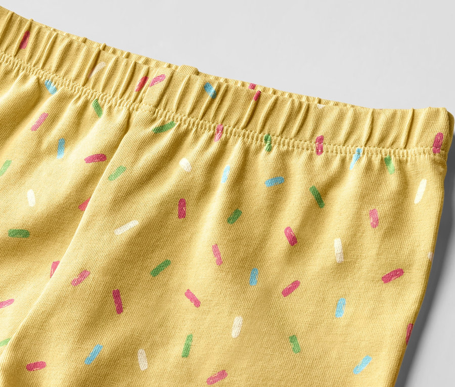 Détail de 2 leggings ¾ pour enfant, rose/jaune, avec motif de décorations colorées.