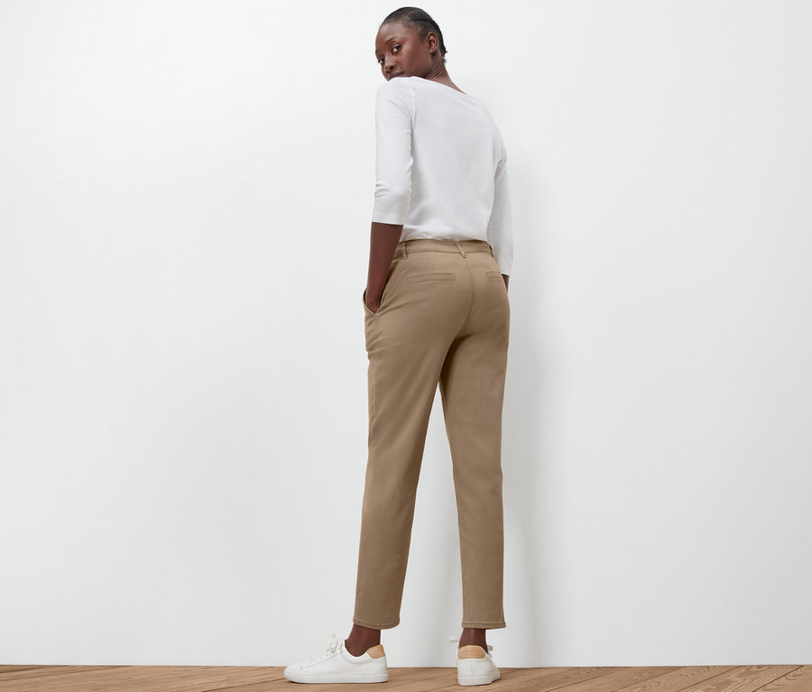 Une femme pose, dos à la caméra, portant un pantalon chino beige.