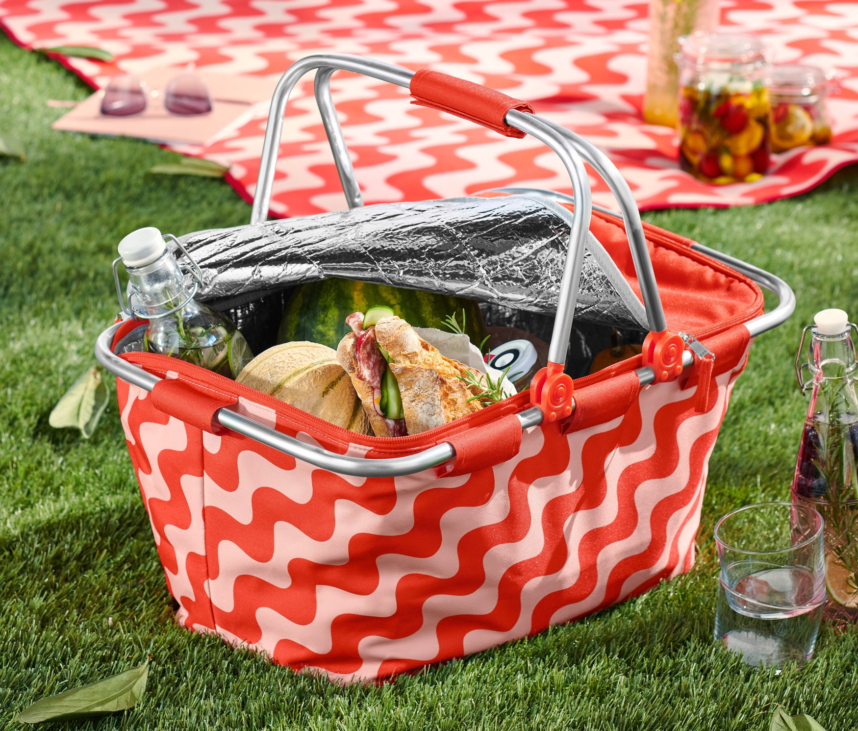 Un panier isotherme rempli de nourriture et de boissons est posé sur l'herbe.