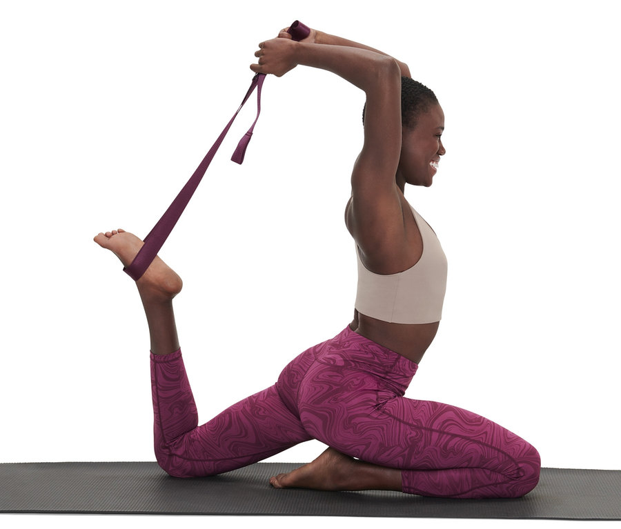 Femme utilisant une ceinture de yoga 2 en 1 violette pour s'étirer sur un tapis.