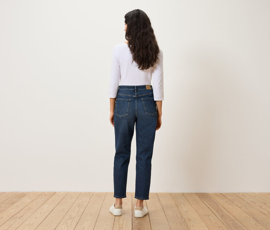 Vue arrière d'une femme aux cheveux foncés portant un jean bleu, un t-shirt blanc et des chaussures blanches.