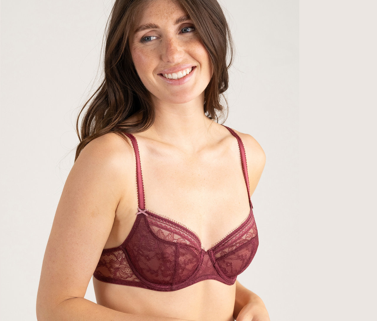 Une femme souriante porte un soutien-gorge en dentelle bordeaux.