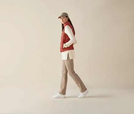 Femme marchant portant un gilet matelassé sans manches, un haut à manches longues, un pantalon et une casquette de baseball.