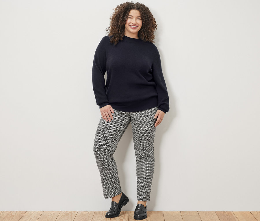 Une femme souriante pose en pull en maille fine bleu foncé et pantalon stretch imprimé.