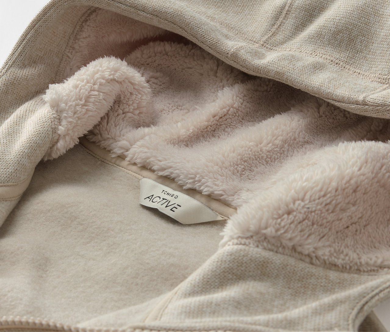 Gros plan d'un sweat à capuche beige avec une doublure en polaire et une étiquette ACTIVE.