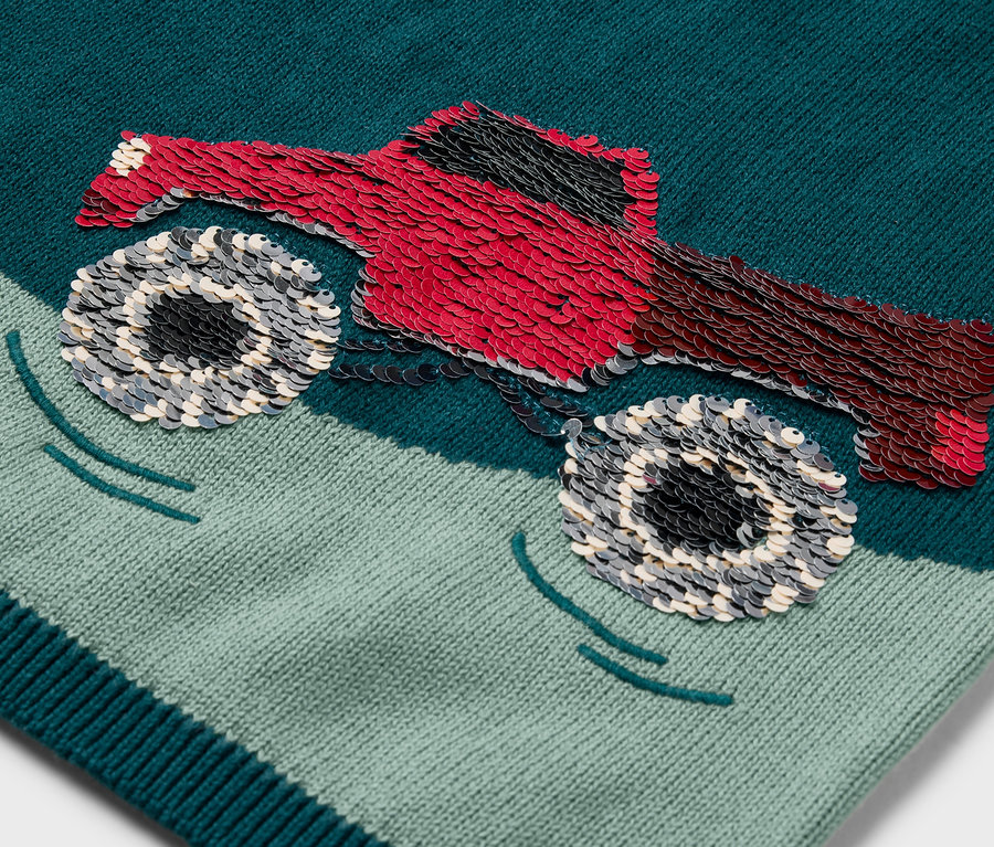 Gros plan sur un pull en maille pour enfant avec un patch de monster truck rouge.