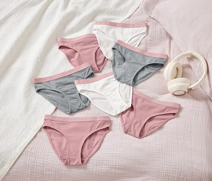 Sur un lit, plusieurs culottes pour femmes de différentes couleurs sont disposées à côté d'un casque audio.