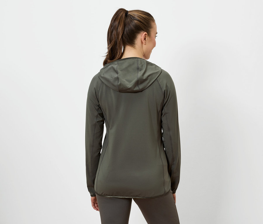 Une femme aux cheveux bruns attachés en queue de cheval porte une veste à capuche vert olive et un legging vert olive.