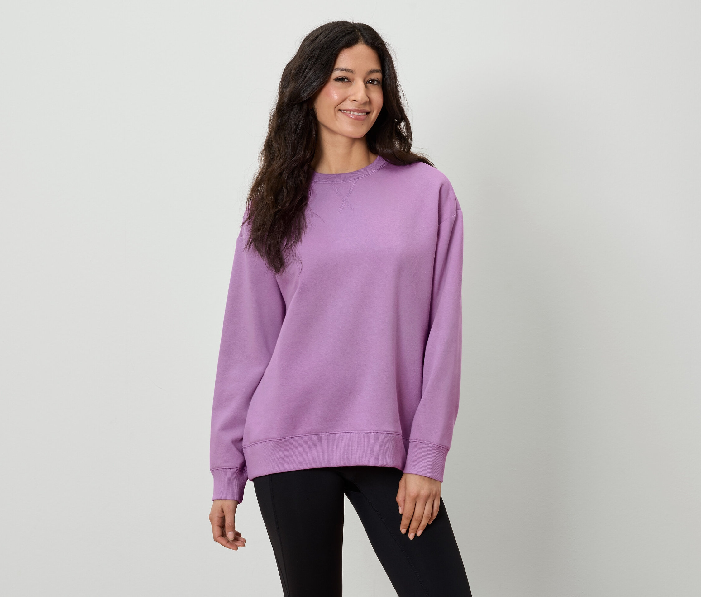 Une femme aux longs cheveux bruns porte un sweat-shirt violet et un pantalon noir.