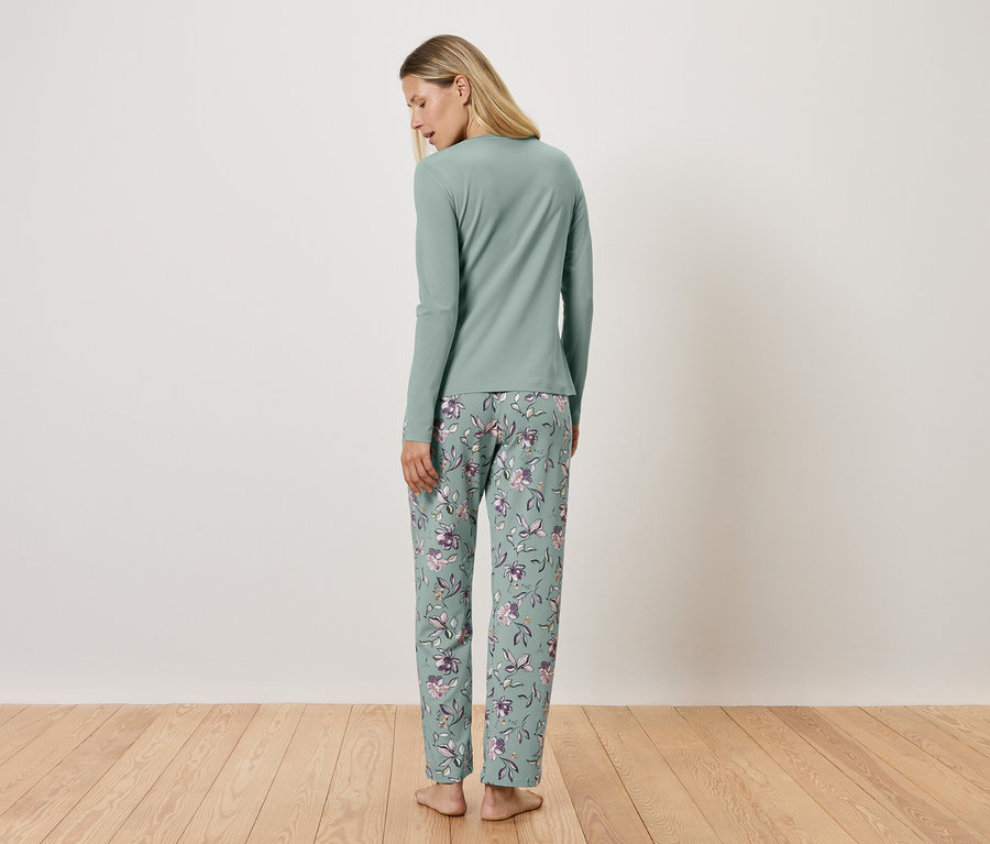 Une femme se tient dos à la caméra et porte un pyjama vert clair à manches longues et un pantalon à fleurs.