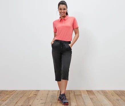 Une femme debout pose dans un polo corail et un corsaire fonctionnel softshell.