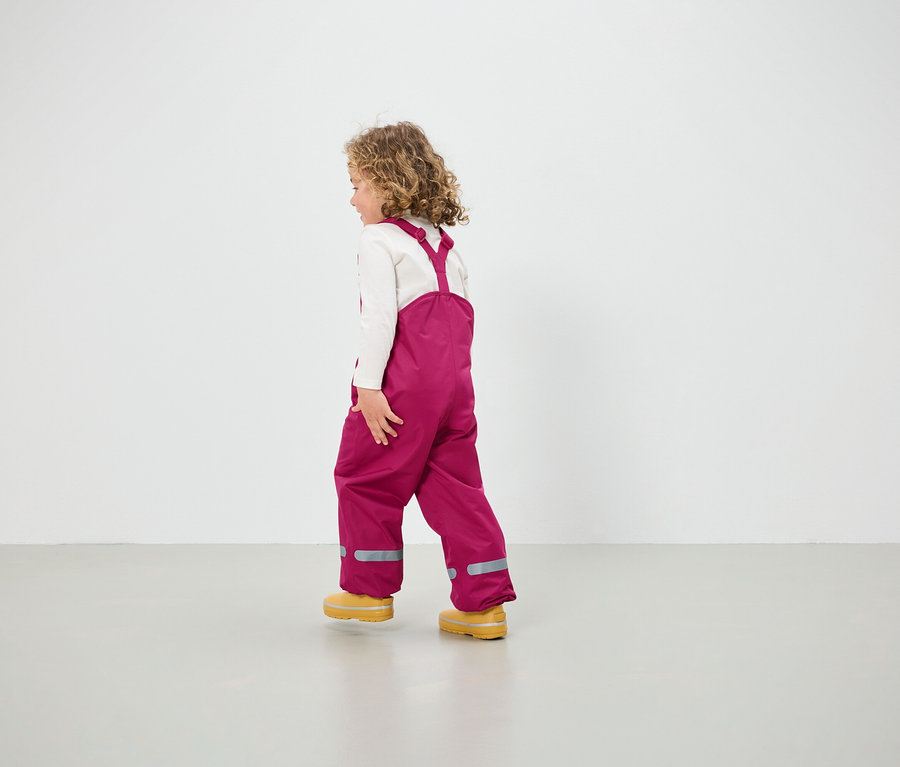 Une fille portant une salopette rose et des chaussures jaunes marche sur le sol.