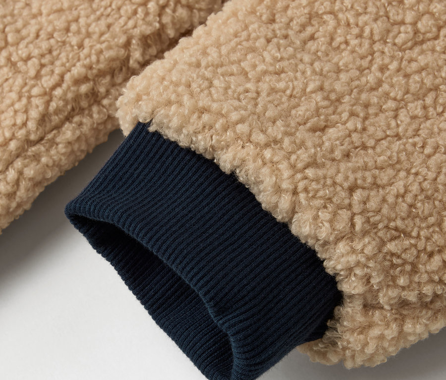 Détail d'une veste réversible pour enfant avec un extérieur beige et un bord de manche bleu foncé.