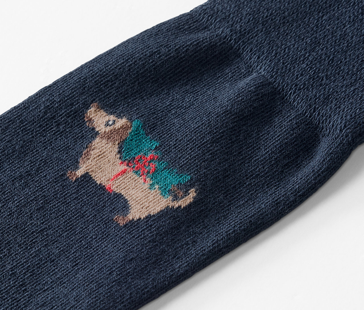 Gros plan d'une chaussette bleue brodée d'un hérisson portant un arbre de Noël.