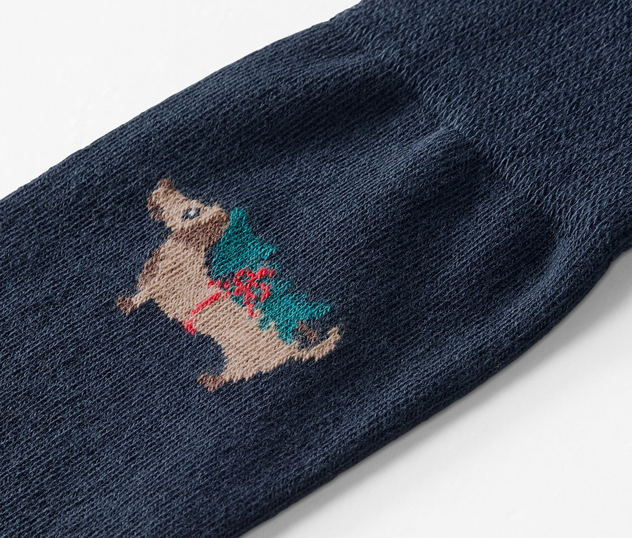Gros plan d'une chaussette bleue brodée d'un hérisson portant un arbre de Noël.