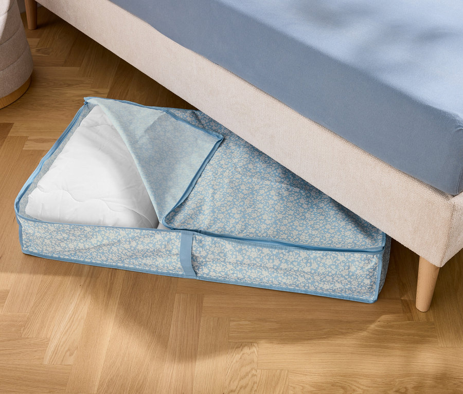 Un sac de rangement bleu avec un rembourrage blanc est situé sous un lit.