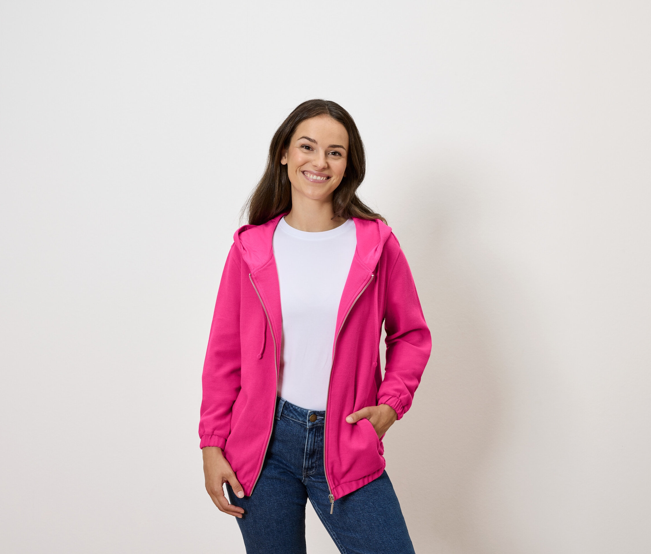Une femme porte un sweat-shirt fuchsia zippé sur un t-shirt blanc et un jean.