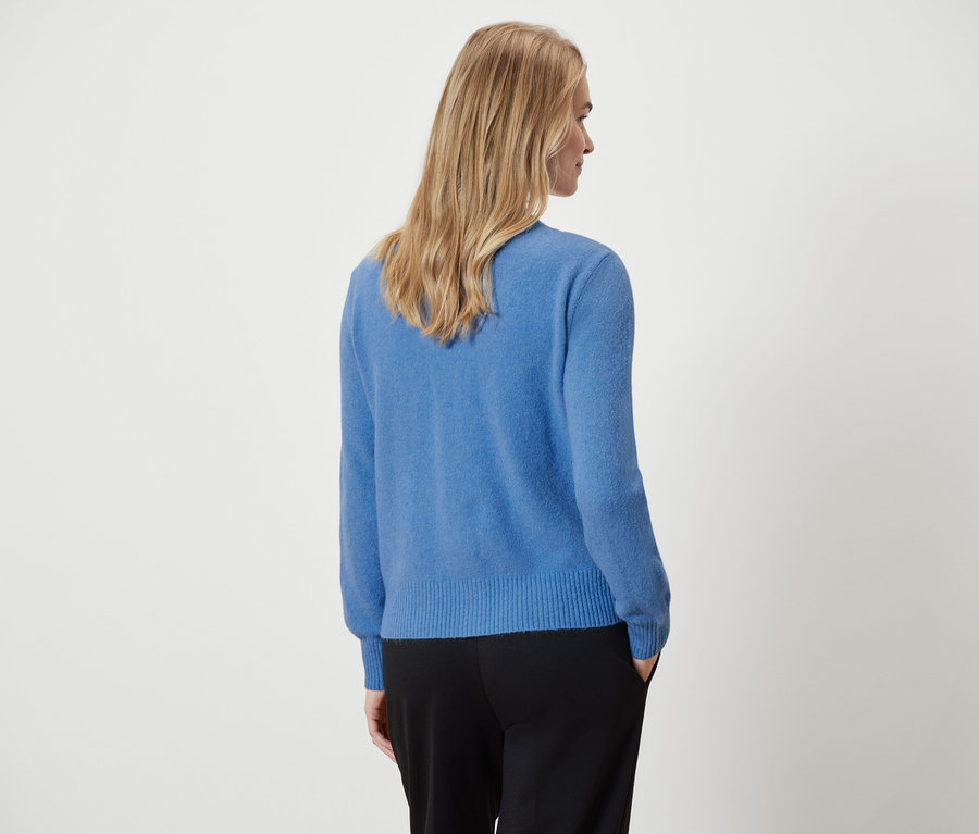 Sur la photo, une femme vue de dos porte un pull bleu et un pantalon noir.