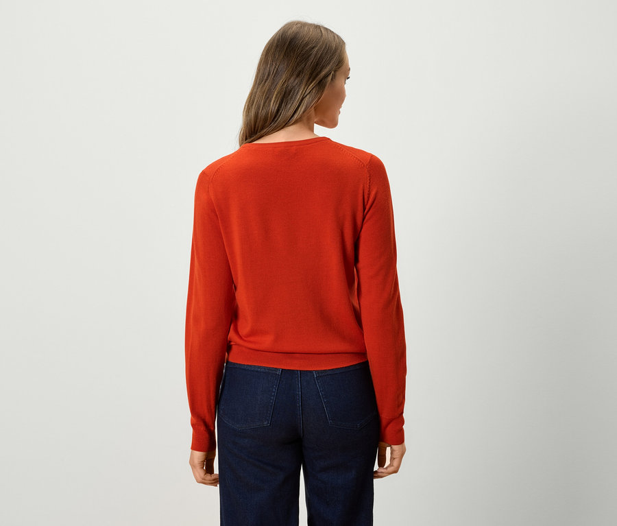 Vue de dos d'une femme portant un pull orange et un jean bleu foncé.