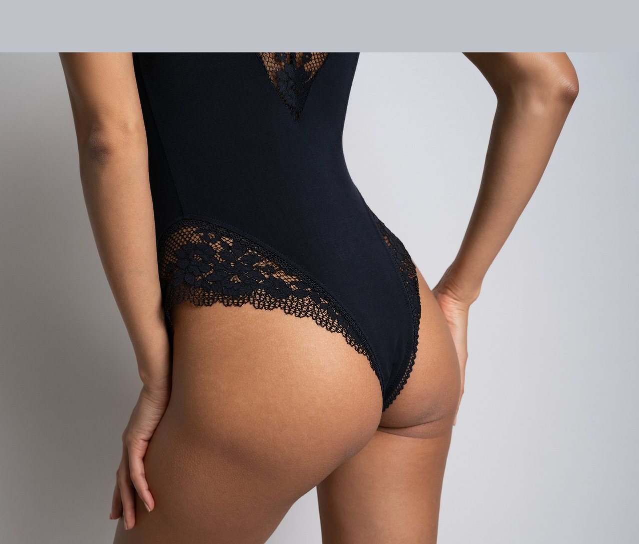 Vue de dos d'une personne portant un body noir Passionata « Nina » avec des détails en dentelle au dos et sur les côtés.