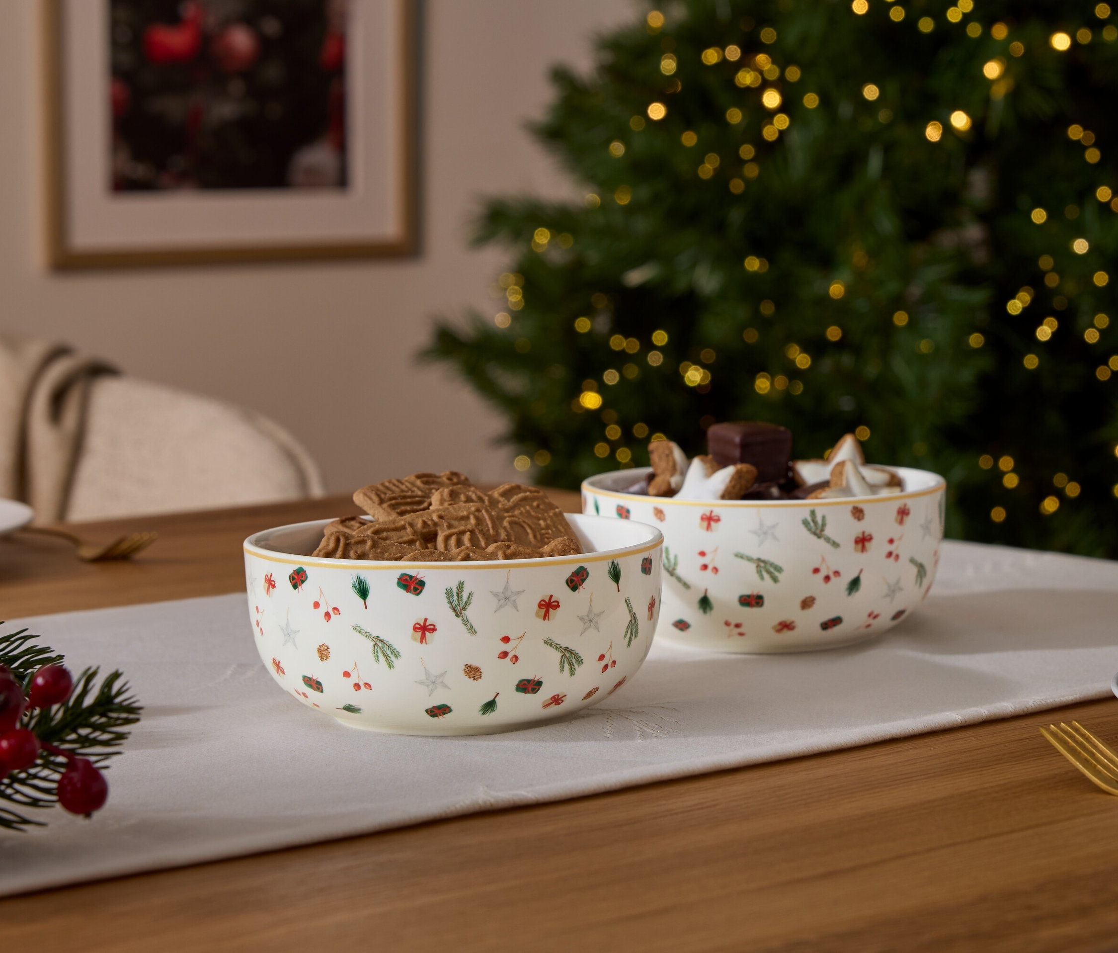 Deux bols à motifs de Noël, l'un rempli de pain d'épices, l'autre de chocolat et d'étoiles, sur une table avec des décorations de Noël.