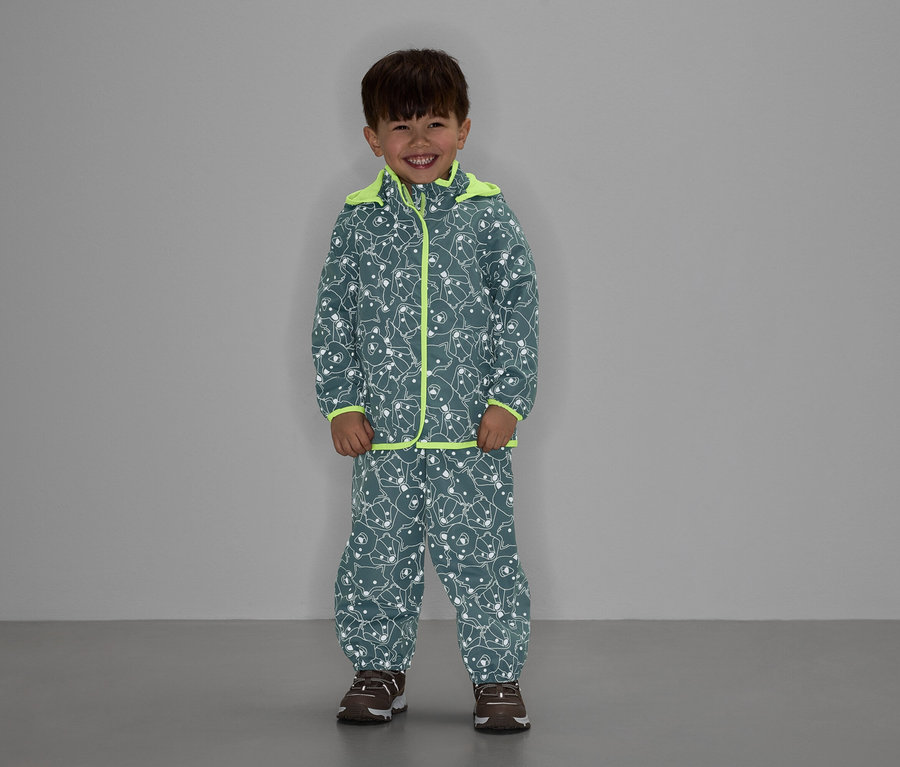 Un garçon souriant porte une veste et un pantalon gris à motif d'ours avec des détails jaune néon.