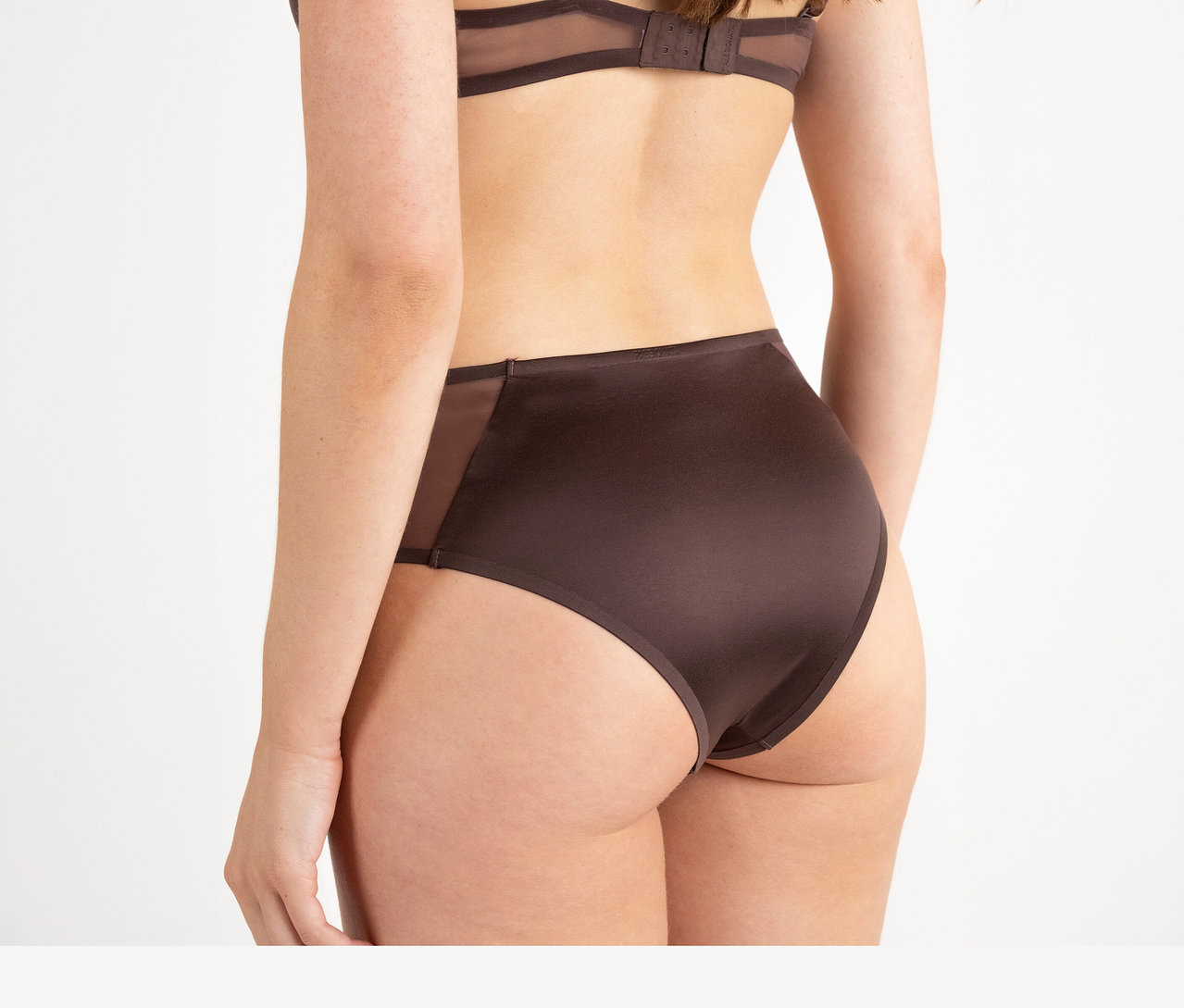 Femme vue de dos portant un soutien-gorge marron chocolat foncé et un slip taille haute Passionata « Bianca » chocolat noir avec empiècements latéraux transparents.