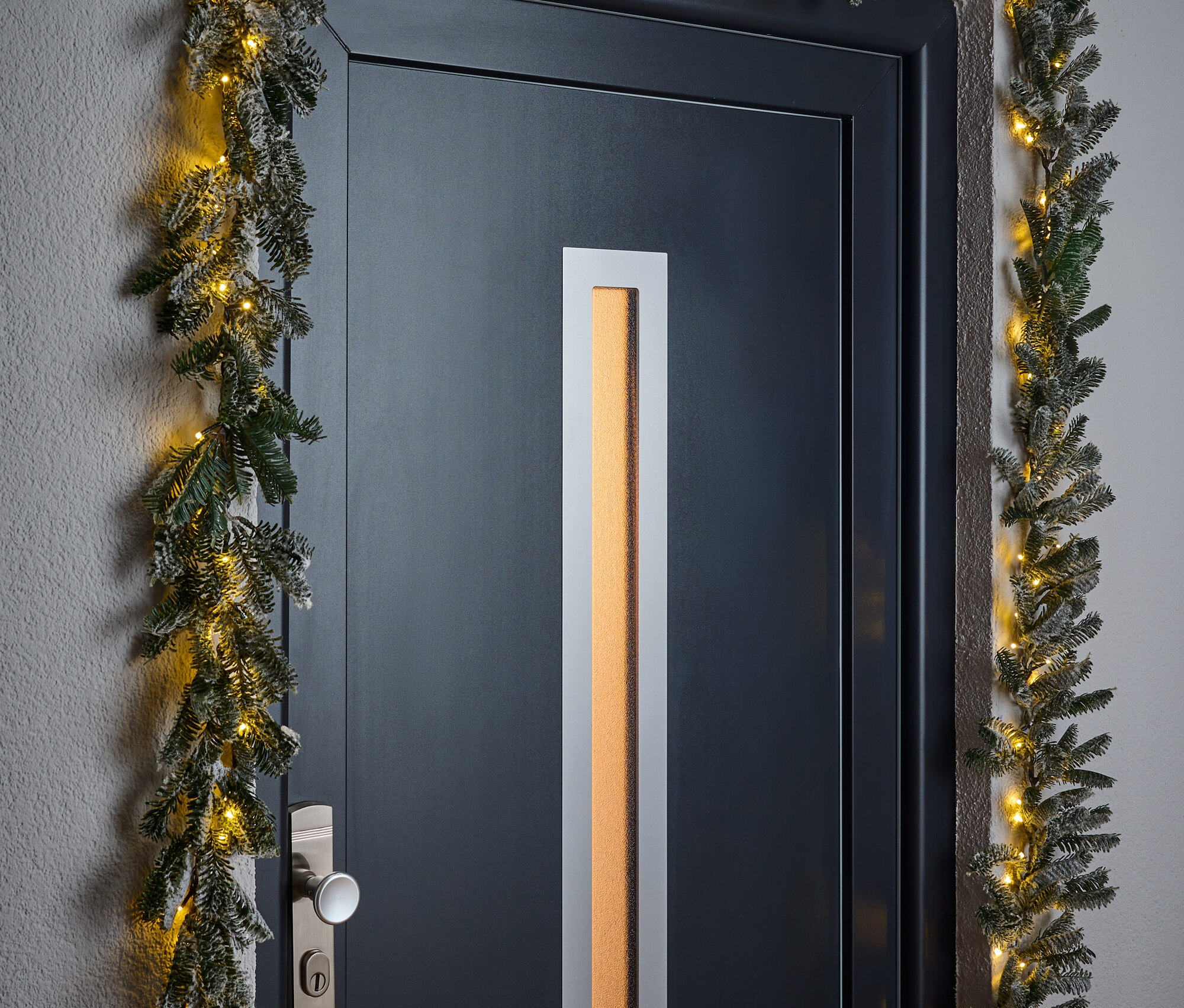 Une porte noire encadrée d'une guirlande de Noël avec de petites lumières.