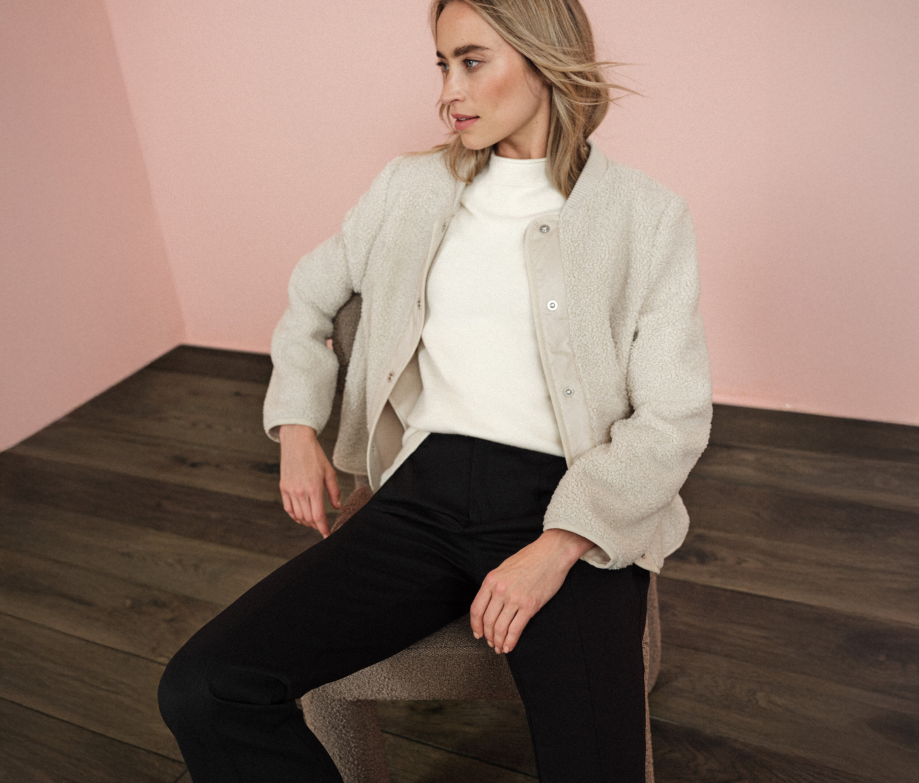 Femme assise portant une veste en teddy avec capuche amovible Street One, un pull à col roulé blanc et un pantalon noir.