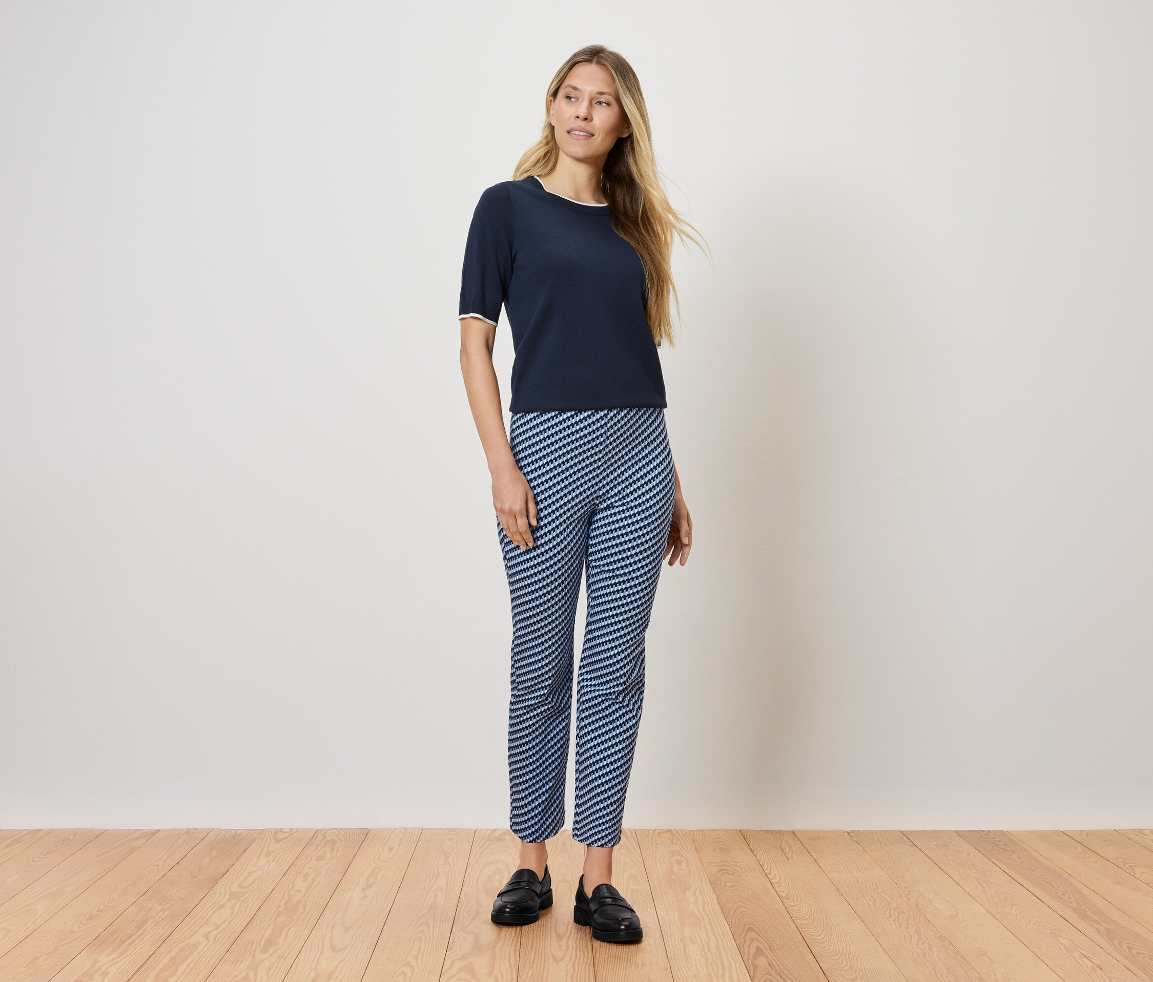 Une femme se tient sur un plancher en bois, portant un t-shirt bleu marine et un pantalon rayé bleu et blanc.