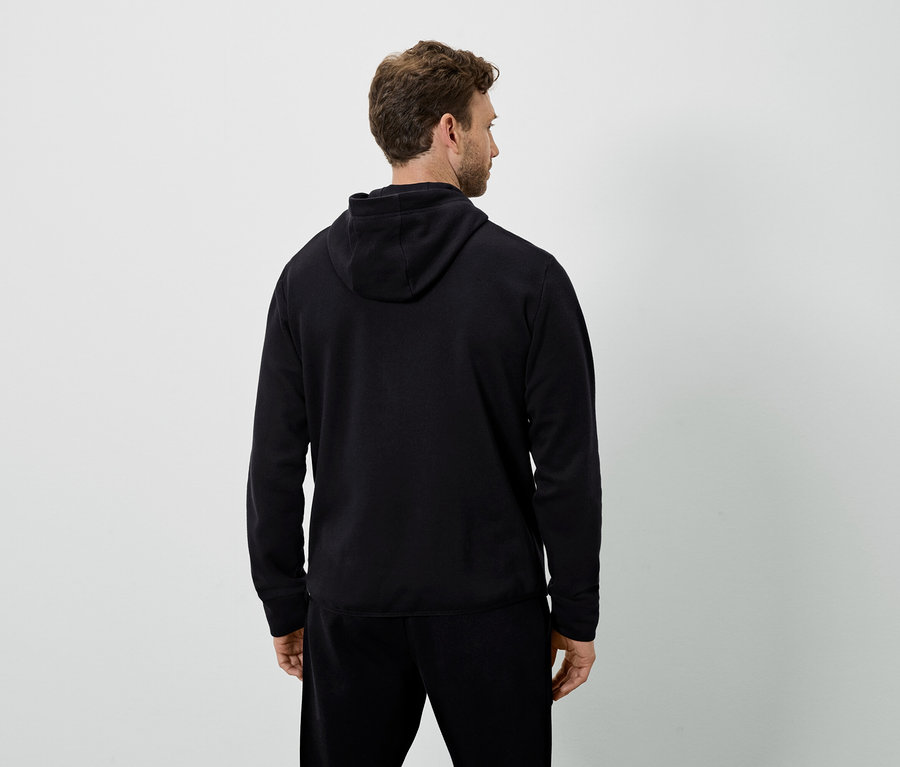 Un homme, vu de dos, porte un sweat à capuche noir et un pantalon de survêtement noir.