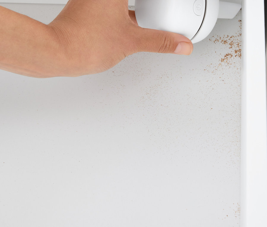 Une main tient un nettoyant sphérique blanc dans une armoire blanche.