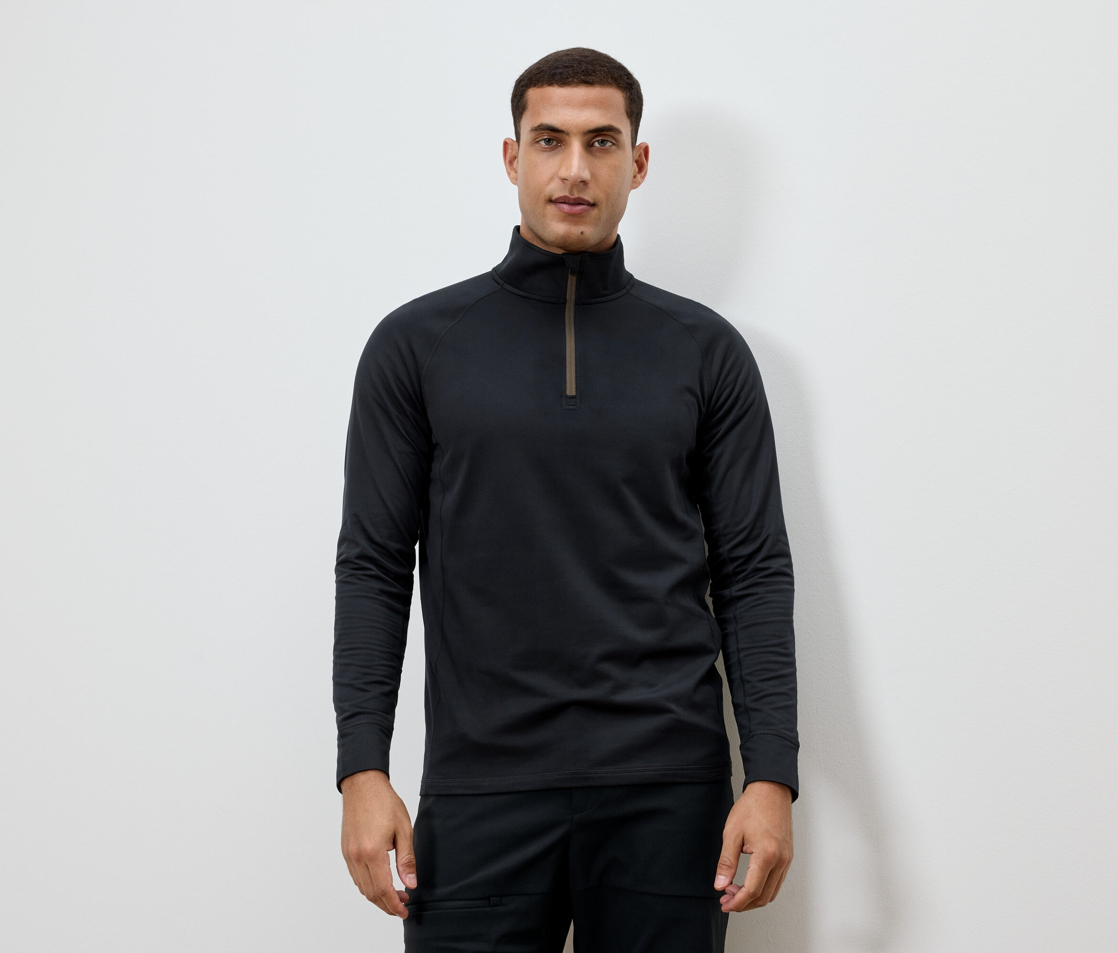 Un homme porte un t-shirt noir à manches longues avec une fermeture éclair au niveau du cou.