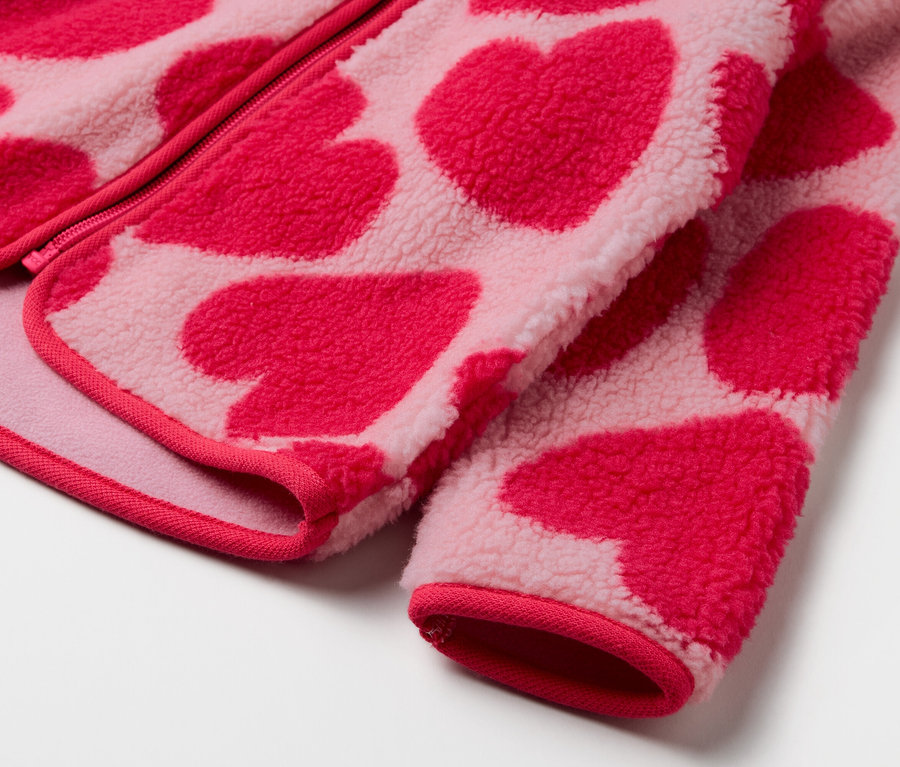 Gros plan sur une veste en polaire rose à motif de cœurs rouges.
