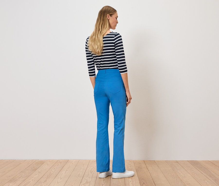 Une femme, vue de dos, porte un pantalon bleu et un t-shirt rayé.