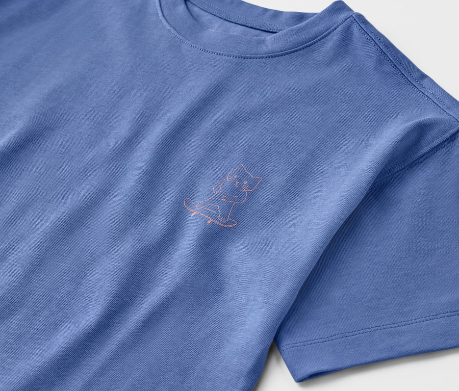 T-shirt heavy bleu pour enfant avec épaules tombantes et un dessin de chat sur un skateboard.