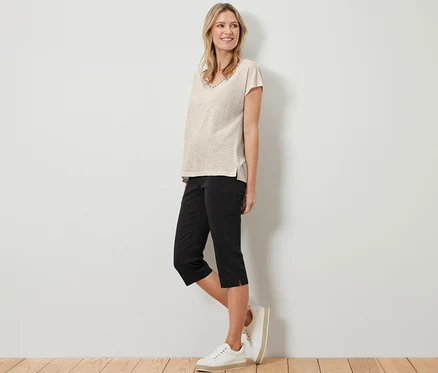 Une femme debout portant un t-shirt beige et un pantalon 3/4 stretch noir.