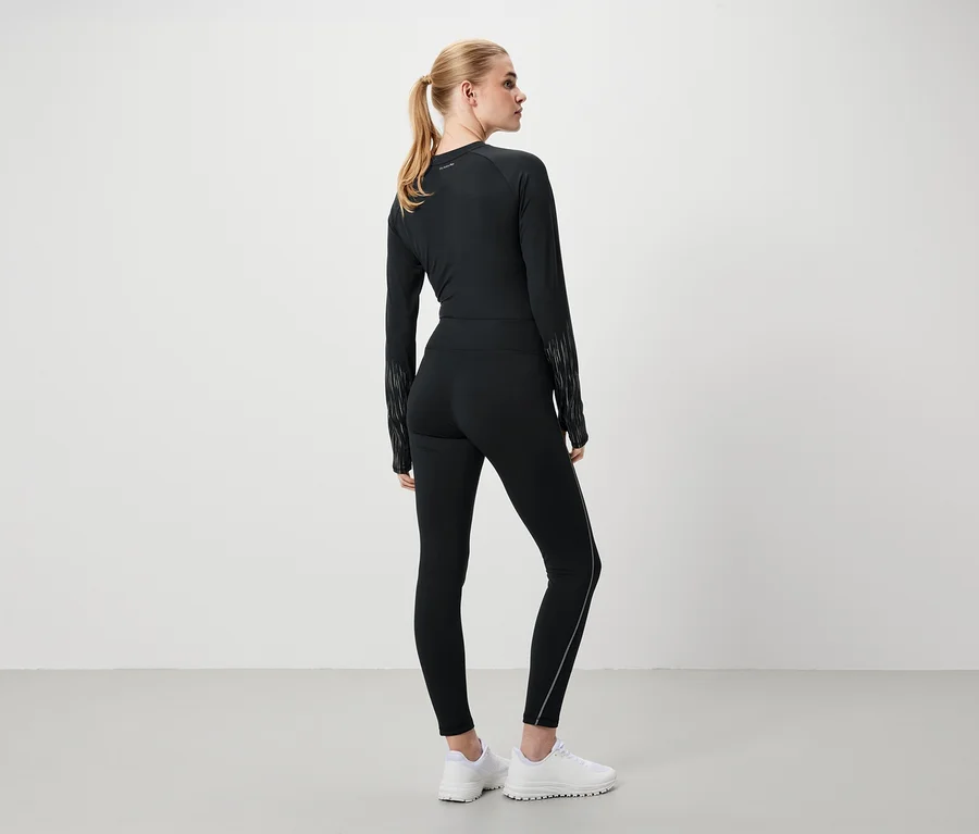 Une femme en tenue de sport noire et chaussures blanches, dos à la caméra.