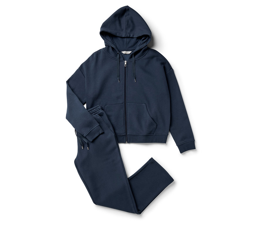 Un sweat à capuche zippé bleu marine et un pantalon de survêtement posés sur un fond blanc.