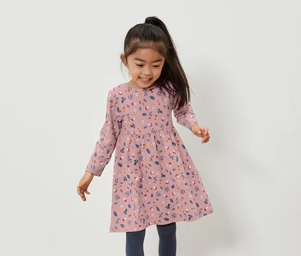 Fillette asiatique souriante portant une robe rose à motifs floraux et des leggings bleus.
